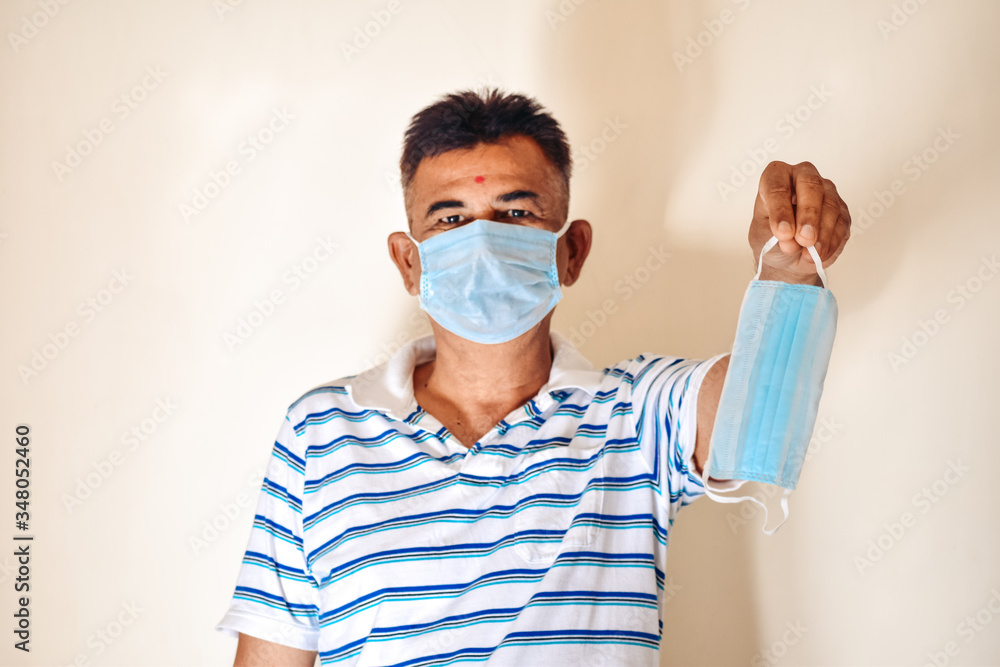 Portrait of adult Indian male wearing medical mask and holding mask in hand. Concept of preventive measures of pandemic disease covid19.