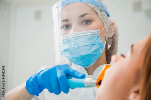 Young female dentist curing patient's teeth filling cavity