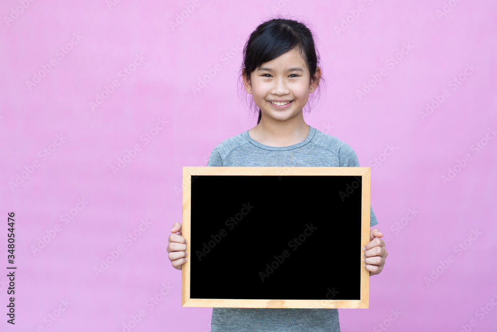 Little asian girl holding blackboard isolated on pink background.