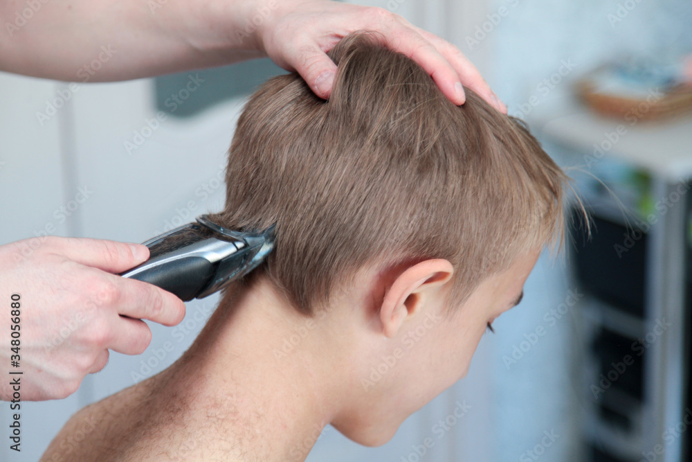 Blond boy gets haircut at home during quarantine isolation. Father cuts his with hair clipper. Stay home concept. Horizontal shot Blond boy gets haircut at home during quarantine isolation. Father cuts his with hair clipper. Stay home concept. Horizontal shot