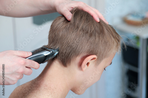 Blond boy gets haircut at home during quarantine isolation. Father cuts his with hair clipper. Stay home concept. Horizontal shot