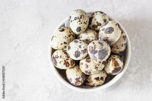 White ceramic bowl with quail eggs, light grey stone background. Selective focus. Top view.