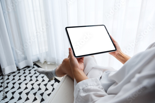 Mockup image of a woman holding black tablet pc with blank white desktop screen while sitting in bedroom with feeling relaxed in the morning © Farknot Architect