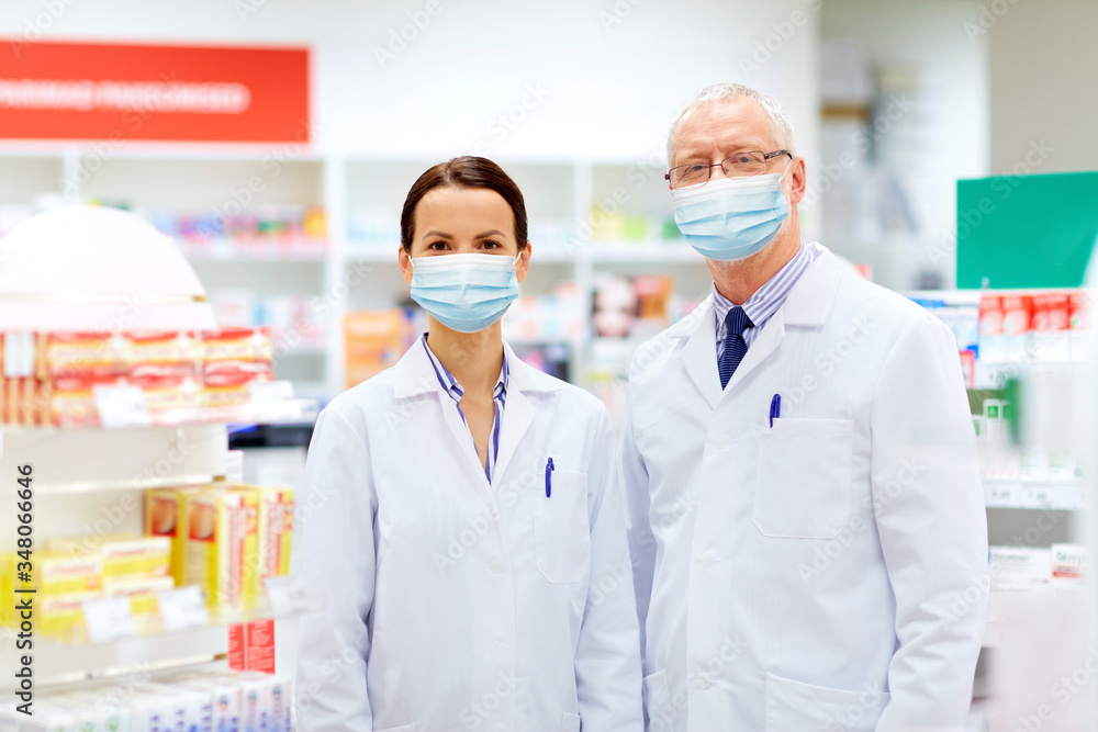 medicine, healthcare and technology concept - happy smiling apothecaries wearing face protective medical mask for protection from virus disease at pharmacy