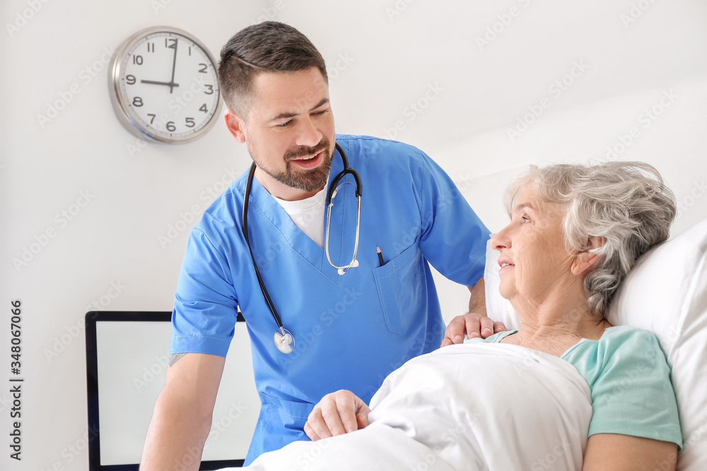 Fototapeta premium Male doctor working with elderly patient in hospital room
