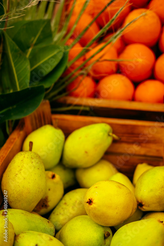 Exotic summer diet. Tropical organic fruit in crate with green leaves. Orange and pear delivery . Autumn harvest. Vertical stock photo.