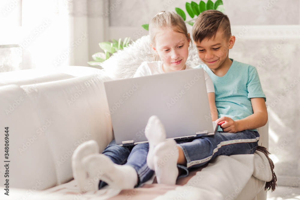 Boy and girl, brother and sister watching a video together on a laptop while sitting on a sofa at home Boy and girl, brother and sister watching a video together on a laptop while sitting on a sofa at home
