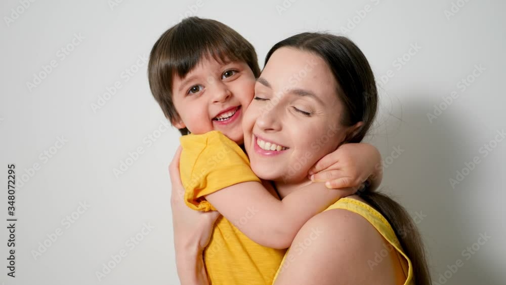 boy hugs his mom tightly dressed in yellow poppies against a white wall in the studio boy hugs his mom tightly dressed in yellow poppies against a white wall in the studio