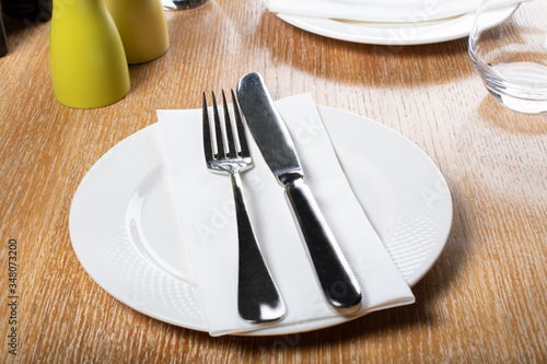 Restaurant table setting with white plate  napkin and cutlery  on wooden table and arrangements