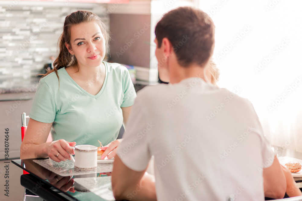 Obraz premium A happy family has breakfast at a table in the kitchen in their apartment. Young woman looking at the camera and smiling