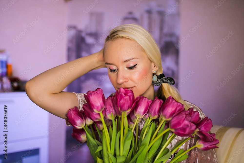Beautiful young blond woman with tulip bouquet. Spring portrait. Bright red flowers in girl's hands. At home. Beautiful young blond woman with tulip bouquet. Spring portrait. Bright red flowers in girl's hands. At home.