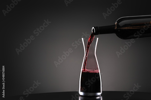 Pouring of tasty wine from bottle into glass on dark background photo