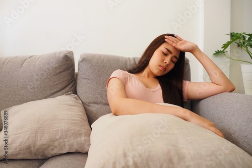 Young Asian woman lying on sofa at home using her hand touching her head feeling tired and stressed about her work and health. Having fever and headache due to insufficient sleep and health problem