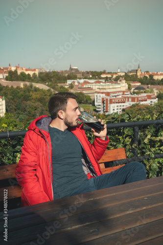 Man drinking beer. Handsome young hipster man drinking beer while sitting at the bar outdoors with panoramic view of Prague