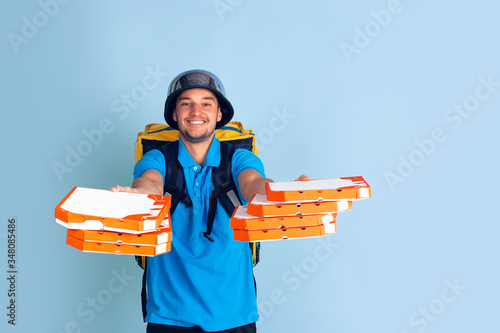 Proposing pizza. Emotions of caucasian deliveryman isolated on blue background. Contacless delivery service during quarantine. Man delivers food during isolation. Safety. Hurrying up. Looks fun. photo