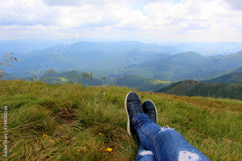 Woman hiker in blue jeans lies on the green grass on the top of Hoverla Mountain in the Carpathians in summer.