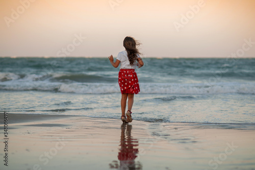 little girl in a red skirt in white peas runs along the seashore