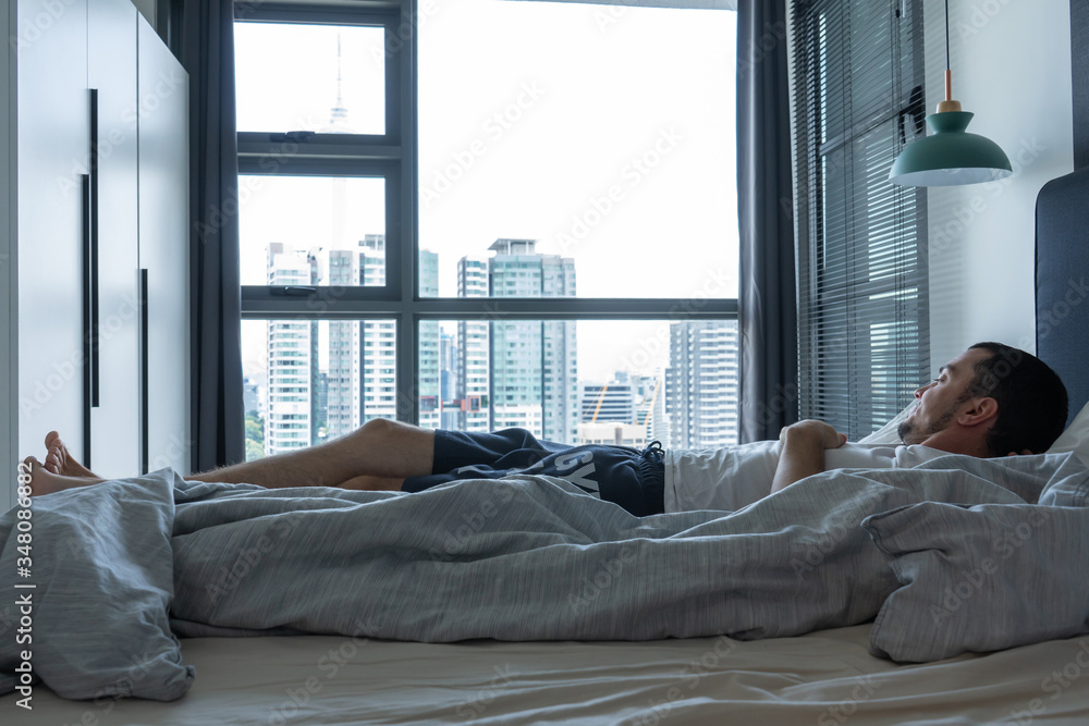 The guy is lying on the bed near the window with excellent breathtaking views of the city from a high floor The guy is lying on the bed near the window with excellent breathtaking views of the city from a high floor