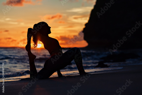 On sunset sea beach sporty young woman doing exercise  stretching to keep feet. Healthy lifestyle dark background. Outdoor sports activity at tropical island yoga spa retreat  family summer vacation.