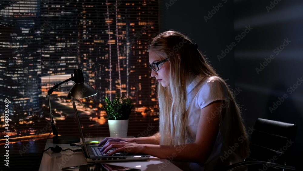 Pretty psychologist searching books in Internet in her office late at night. In the background there are skyscrapers. Pretty psychologist searching books in Internet in her office late at night. In the background there are skyscrapers.