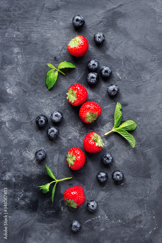 Composition of strawberries and blueberries and mint leaves on a dark concrete background top view