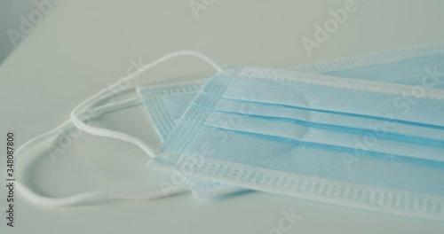 Pan right of two disposable earloop clinical blue face masks on white table photo