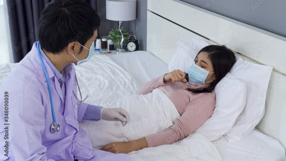 sick woman lying in bed while doctor checking her pulse, people must be wearing medical mask protecting from coronavirus(covid-19) pandemic sick woman lying in bed while doctor checking her pulse, people must be wearing medical mask protecting from coronavirus(covid-19) pandemic