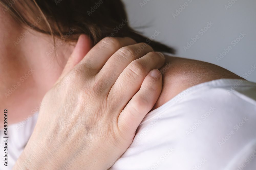 Woman experiences severe pain and discomfort in the neck, she massages the sore spot with her hand.