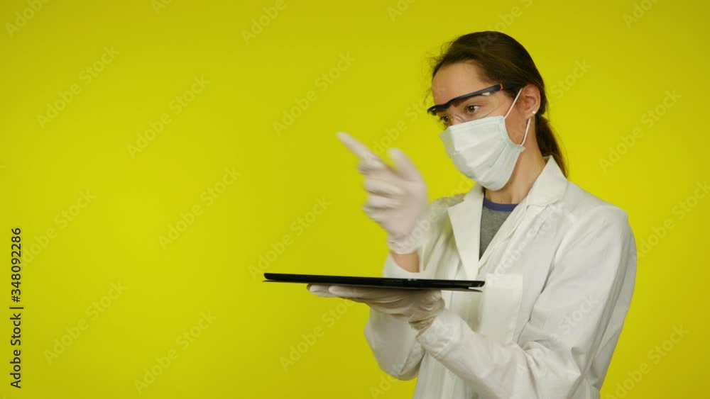 Woman in medical coat and protective mask uses holographic technology of the future on tablet screen. Augmented reality concept. Yellow background with copy space. Place for graphics. 4K footage Woman in medical coat and protective mask uses holographic technology of the future on tablet screen. Augmented reality concept. Yellow background with copy space. Place for graphics. 4K footage