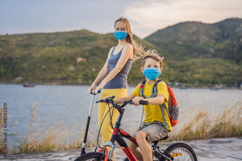 Active school kid boy and his mom in medical mask riding a bike with backpack on sunny day. Happy child biking on way to school. You need to go to school in a mask because of the coronavirus epidemic