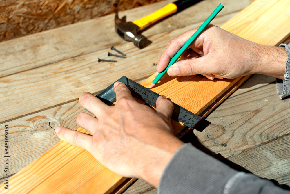 Male carpenter marks with pencil using a square on the board, marks for saw cut. Male hands with pencil and a square close-up on wooden board. Male carpenter marks with pencil using a square on the board, marks for saw cut. Male hands with pencil and a square close-up on wooden board.