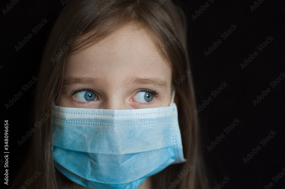 Portrait of sad girl with blue eyes is looking at the camera on black backgound in surgical disposable mask for protection of Coronavirus Covid-19 during self-isolation while staying at home Portrait of sad girl with blue eyes is looking at the camera on black backgound in surgical disposable mask for protection of Coronavirus Covid-19 during self-isolation while staying at home