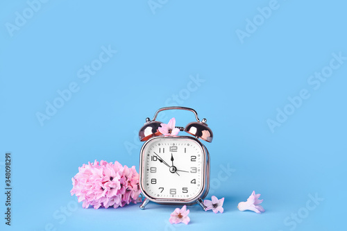 Alarm clock and flowers on color background. Spring time