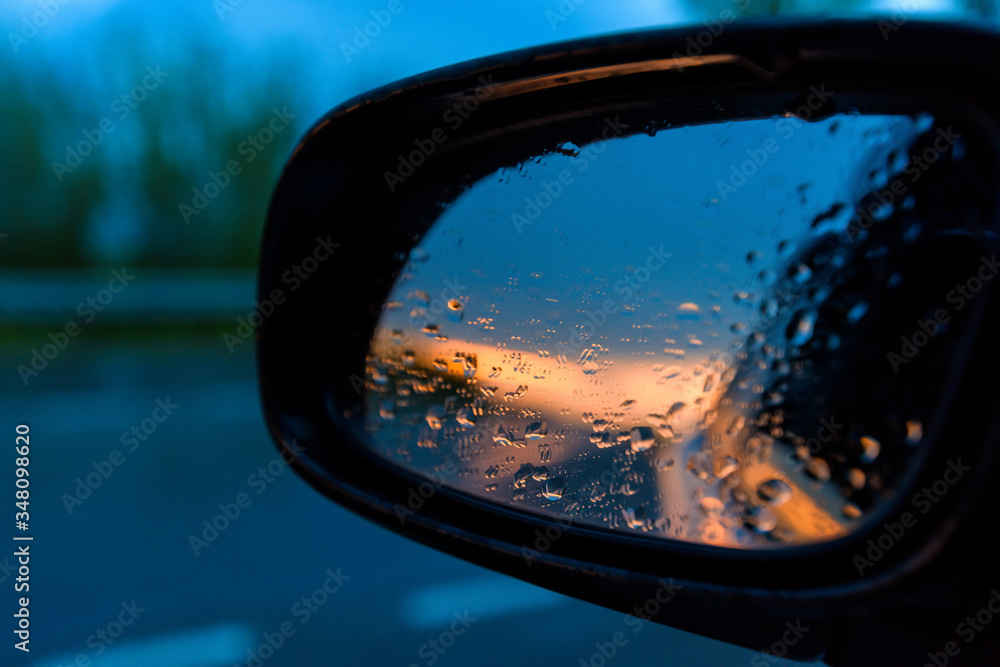 raindrops on the rearview mirror of a car at sunset. the sunset is reflected in the car mirror .