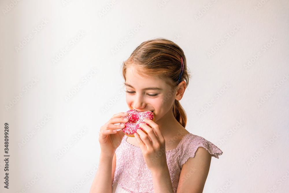 Cute blonde little girl eating pink donut and smiling. Junk food concept. Cute blonde little girl eating pink donut and smiling. Junk food concept.