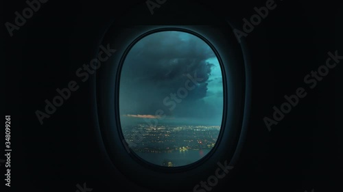 Airplane window view plane flying through storm turbulence with lightning over coastal city