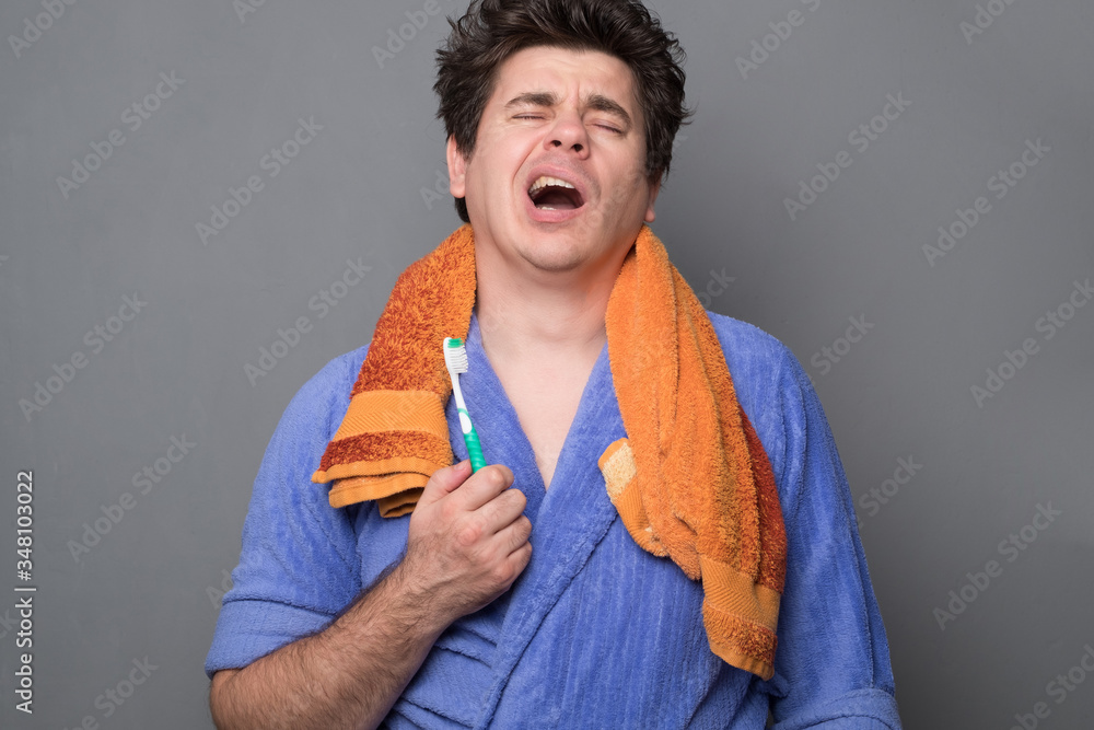 Sleepy man in a bathrobe brushes his teeth in the morning. Man in a bathrobe is holding a towel. Sleepy man in a bathrobe brushes his teeth in the morning. Man in a bathrobe is holding a towel.