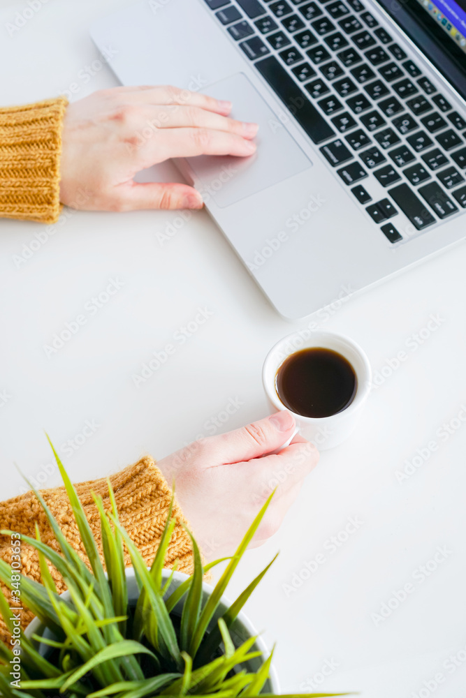 girl holds a coffee mug near a laptop and types on the keyboard