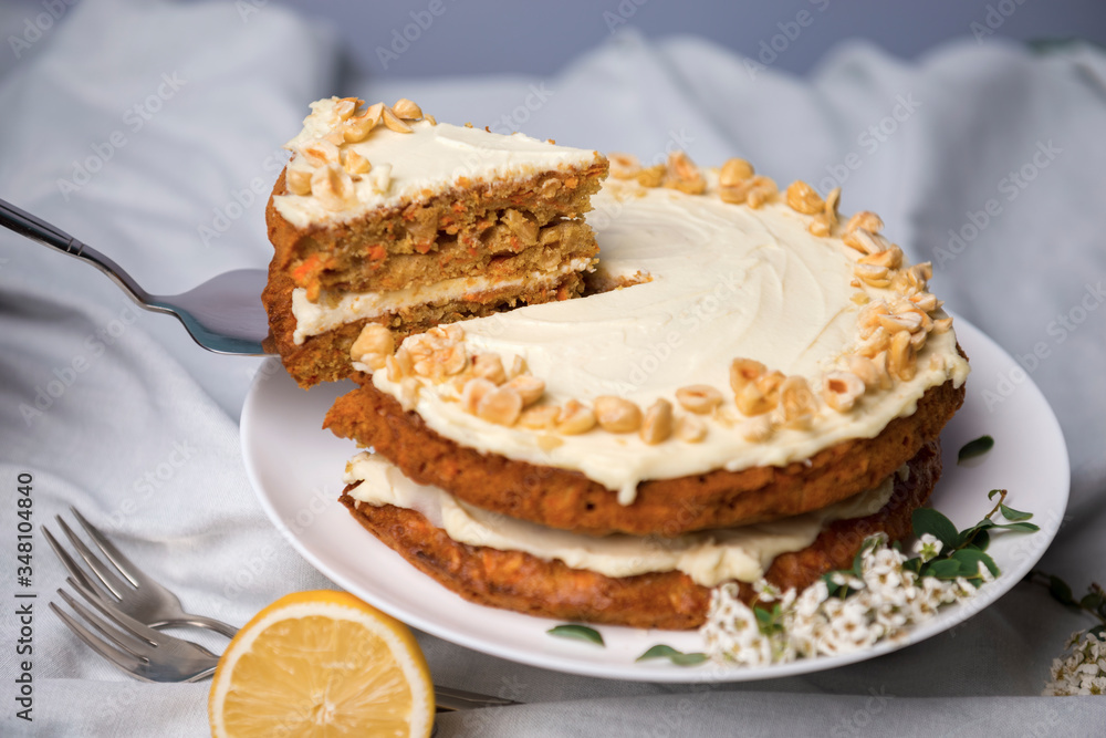 Carrot cake with hazel nuts, decorated with white flowers of meadowsweet and slice lemon on the white tablecloth Carrot cake with hazel nuts, decorated with white flowers of meadowsweet and slice lemon on the white tablecloth