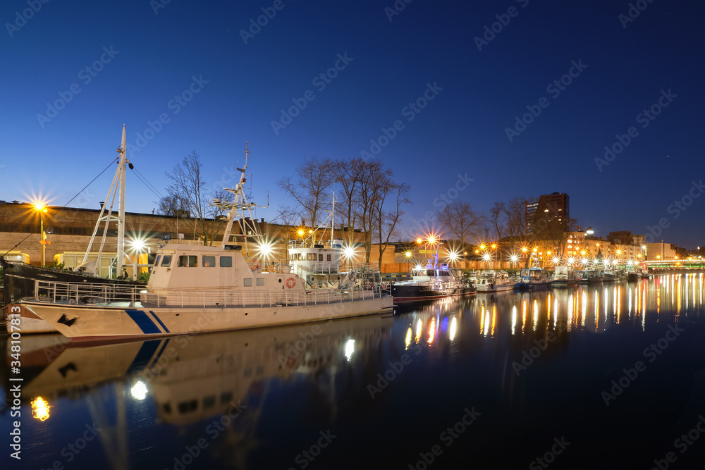 Pier for boats and yachts in Klaipeda, Lithuania, on sunset. Beautiful view of vessels and their reflections in calm water on blue hour