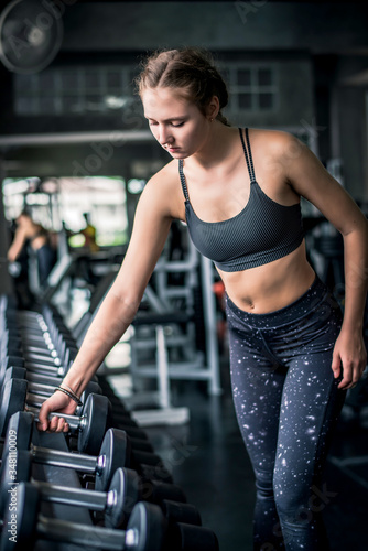 Cinematic tone of young attractive fitness woman exercise with dumbbell in gym. Individual sport to fit muscles of body and workout exercise for healthy life concept.