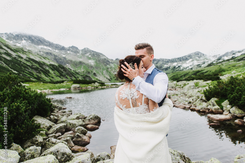 Naklejka premium Beautiful bride and groom hug and kiss in the mountains. Wedding photo session in the mountains.