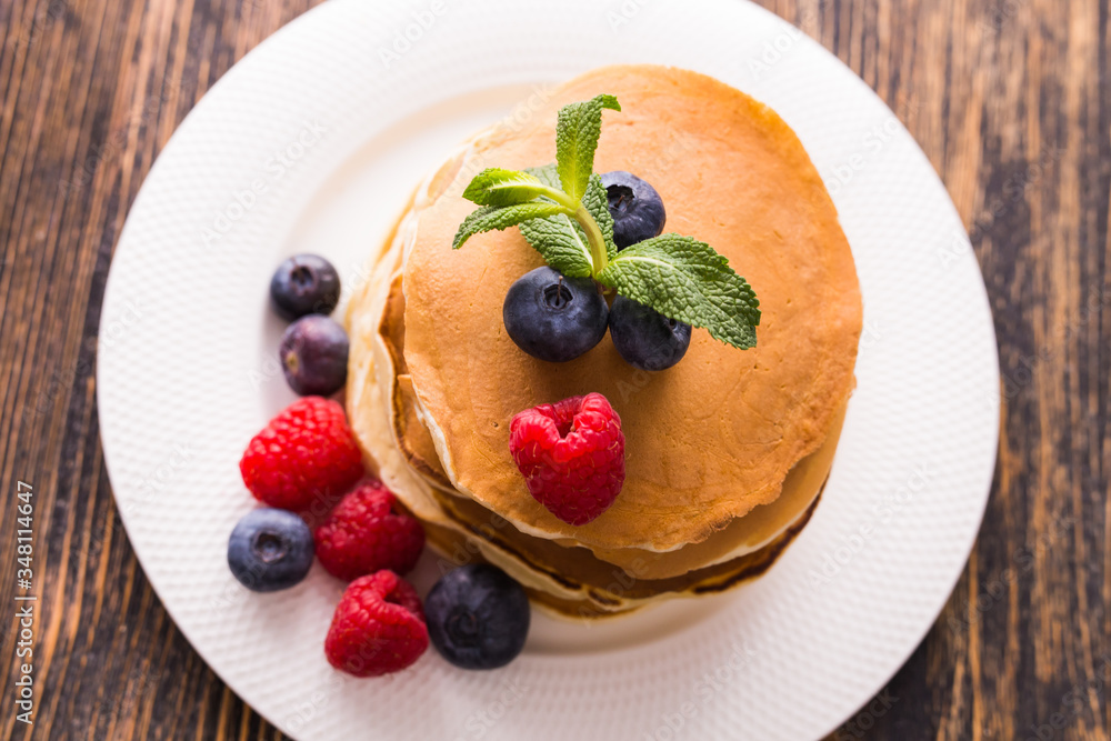 Homemade sweet pancakes with blueberries and raspberries on a white plate, top view. Homemade sweet pancakes with blueberries and raspberries on a white plate, top view.