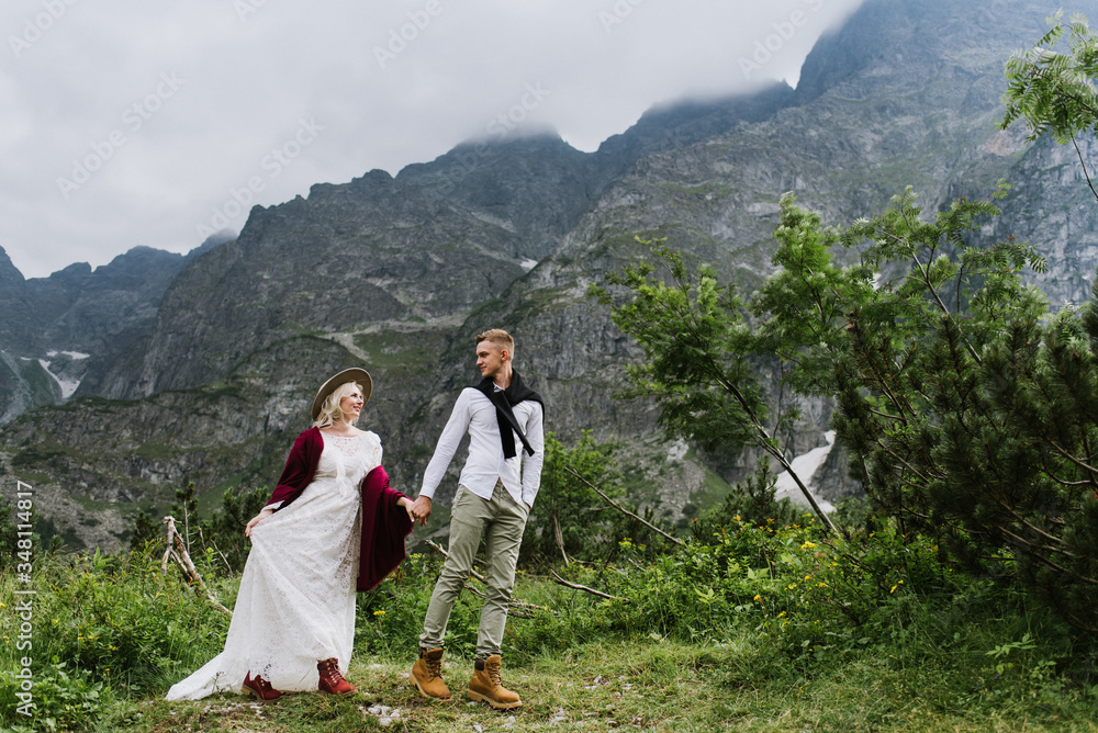 Naklejka premium Beautiful bride in a boho dress and groom walk in the mountains. Wedding photo shoot in the mountains. Black and white photo of a bride and groom in the mountains.