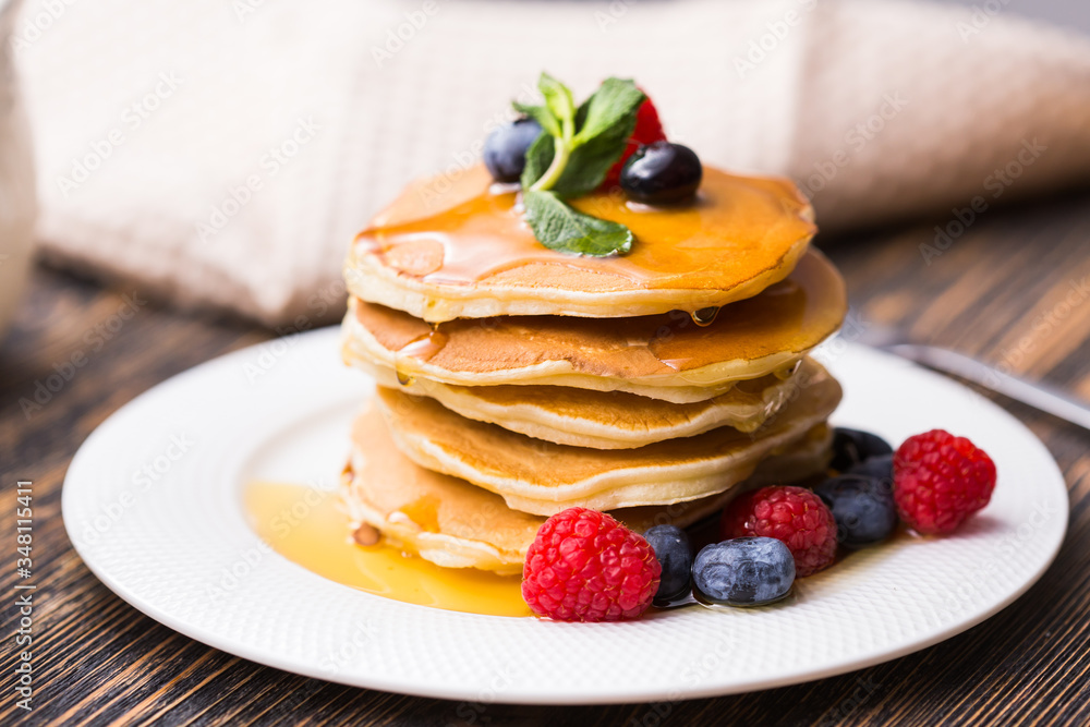 Pancakes with blueberries and raspberry and maple syrup on wooden background. Breakfast and traditional meal. Pancakes with blueberries and raspberry and maple syrup on wooden background. Breakfast and traditional meal.