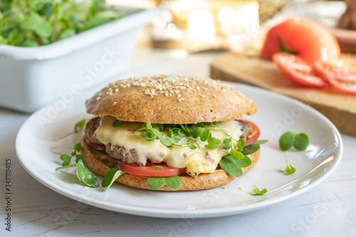 Healthy burger with whole grain buns, beef, cheese and tomatoes on a white plate with microgreens