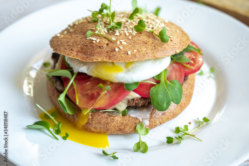 Person hold healthy homemade beef cheese burger with whole grain buns, poached egg, tomatoes and microgreens, healthy food close-up