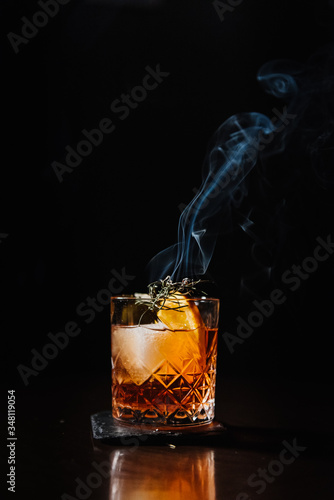 Whiskey with orange, ice and smoking rosemary close-up.