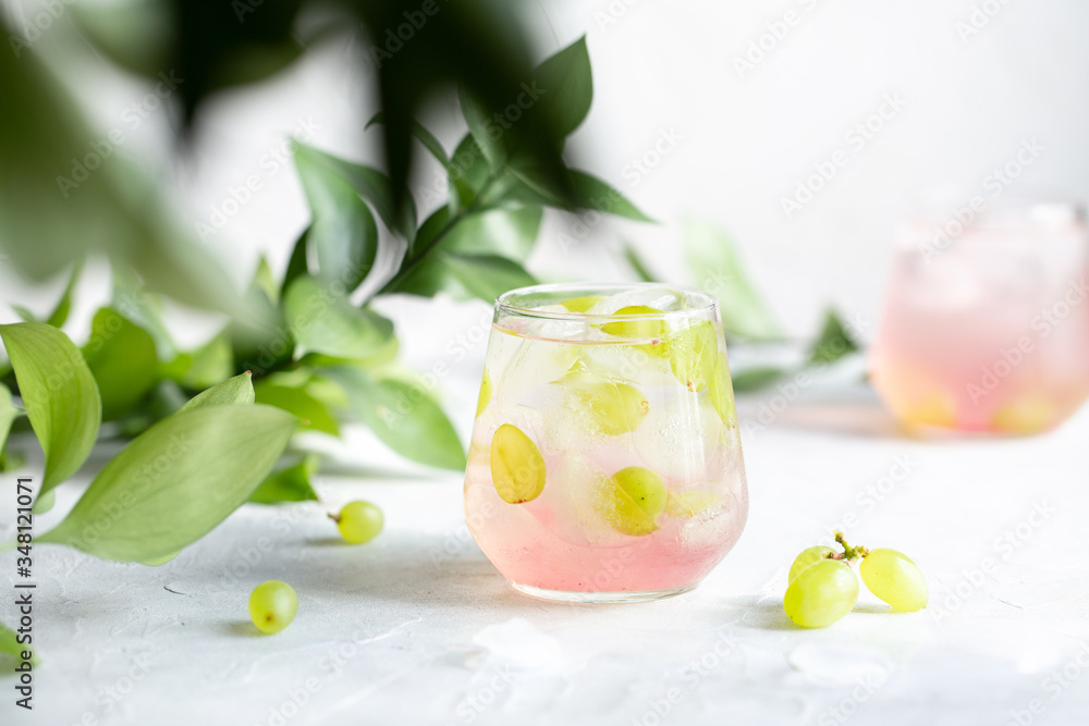 Summer cold lemonade with grapes on a light table among greenery.