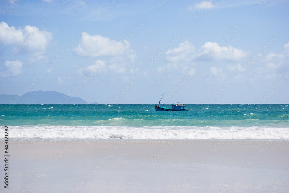 Vietnamese fishing boat in the azure sea with sea waves on a background of blue sky. Doc Let beach